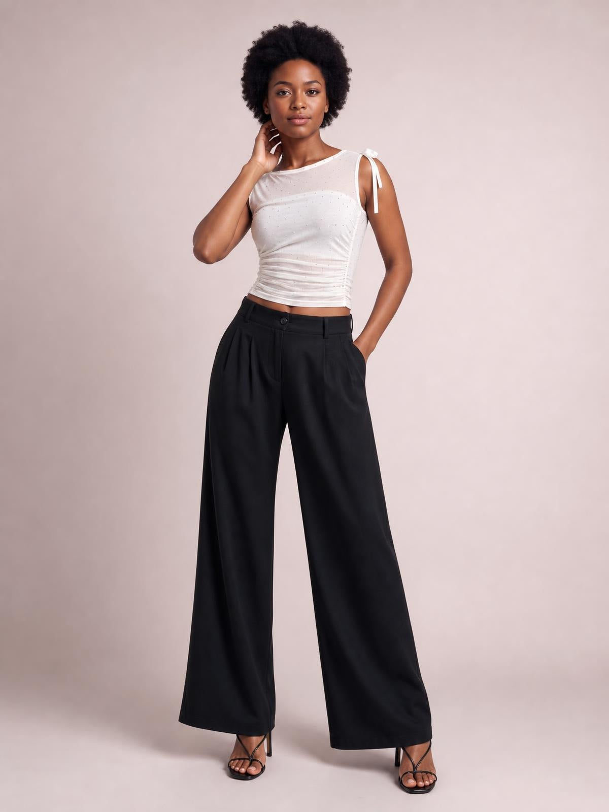 Model wearing black high-waisted wide-leg pants with a button closure and side pockets, standing with one hand in a pocket and one leg angled forward.