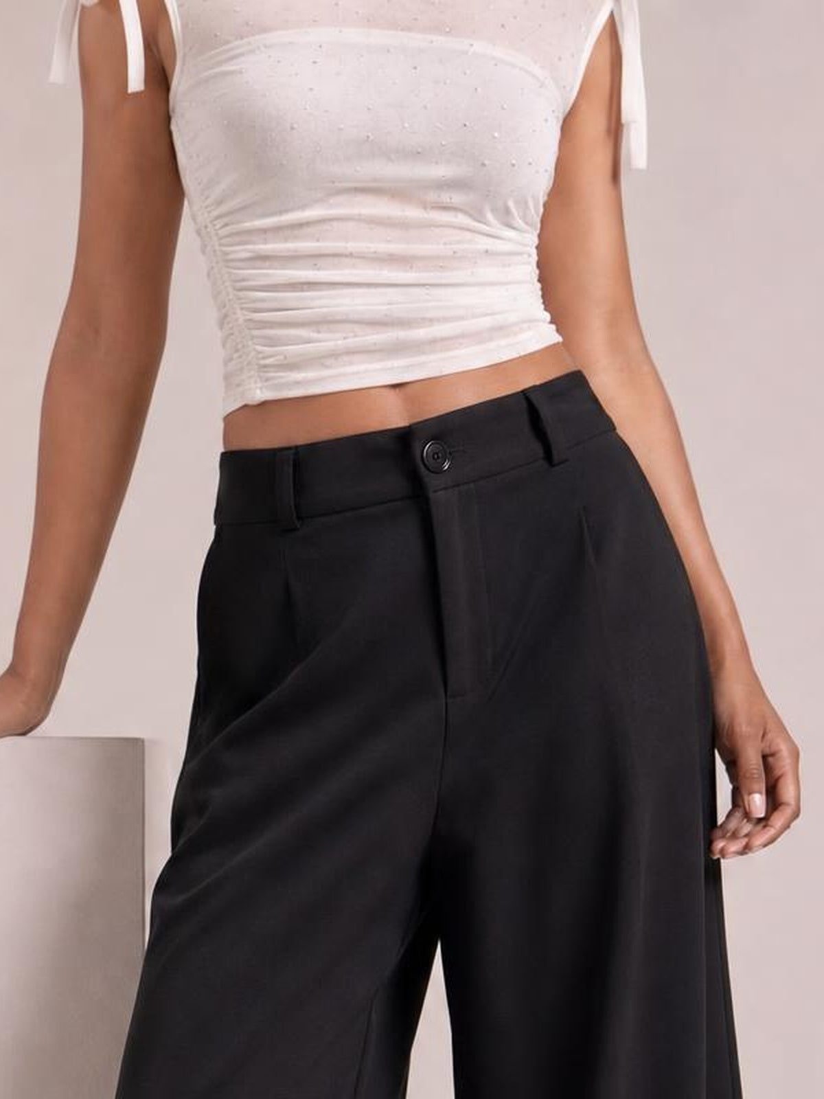 A model wears black high-waisted wide-leg pants with a buttoned waistband, belt loops, front pockets, and a relaxed silhouette.