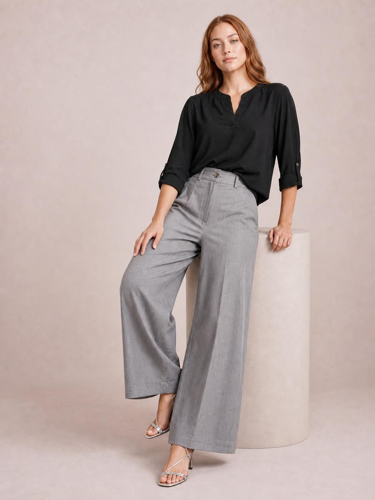 Model poses in gray high-waisted wide-leg pants with a buttoned waistband, belt loops, pockets, and relaxed full-length silhouette.