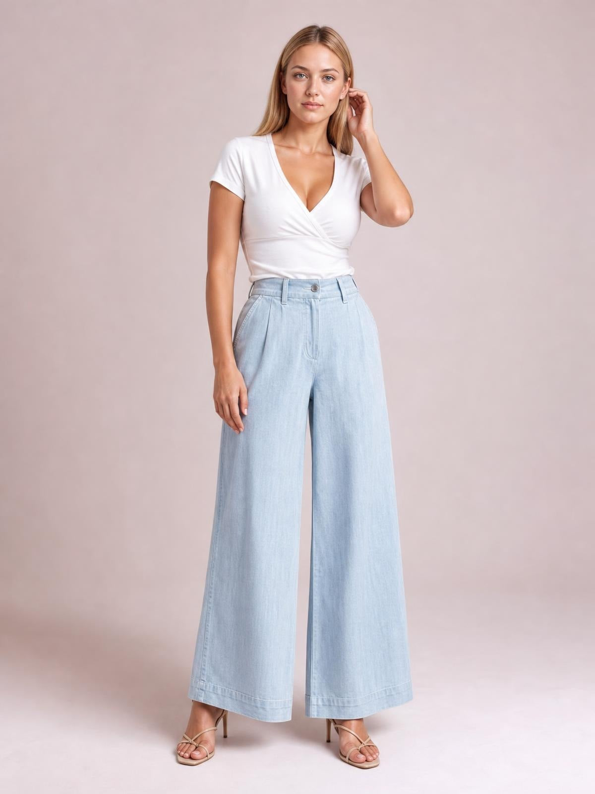 A standing model wears light blue high-waisted wide-leg pants with a button closure, belt loops, side pockets, front pleats, and wide cropped hems.