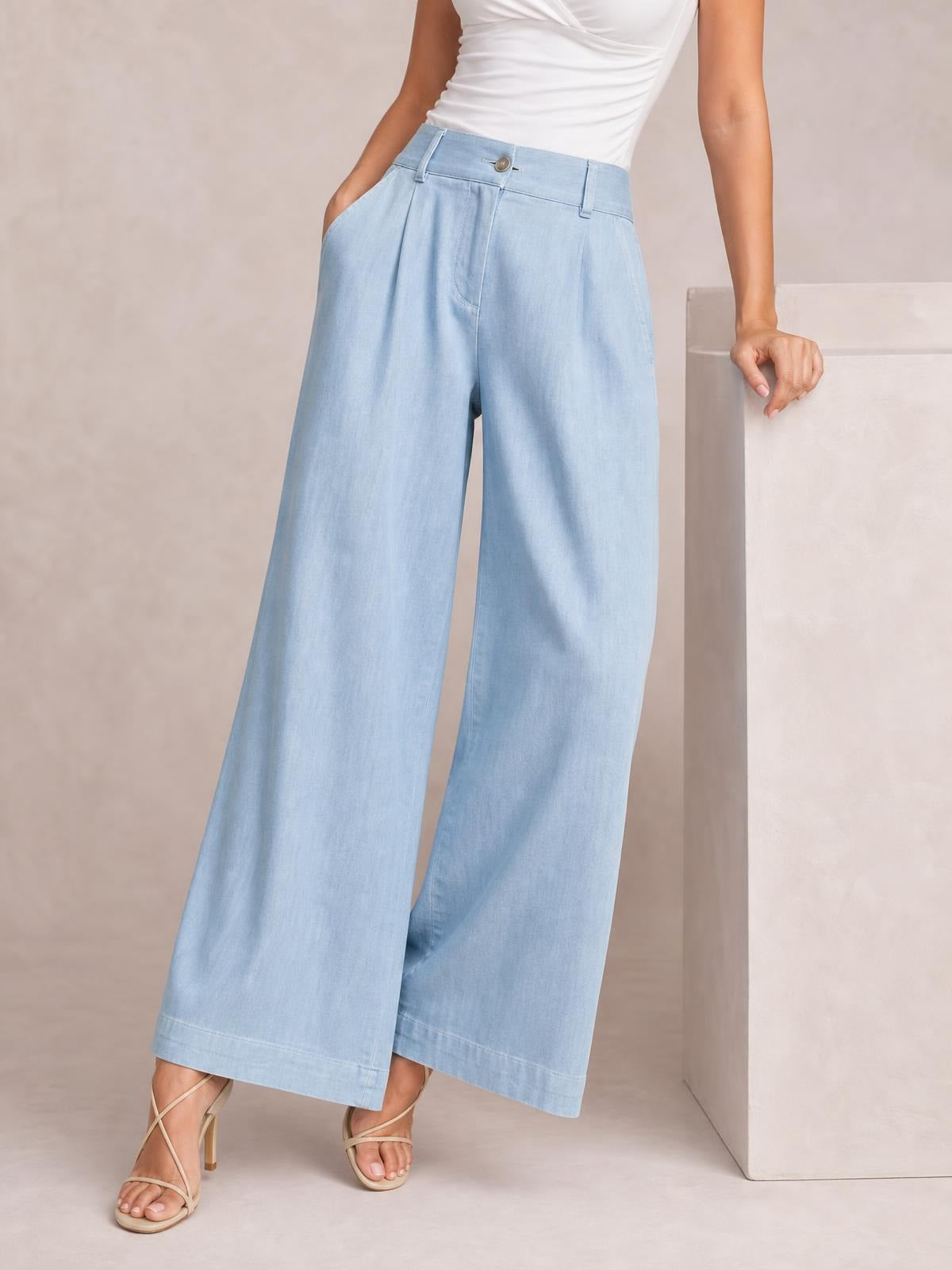 A model wears light blue high-waisted wide-leg pants with a button closure, belt loops, front pockets, and softly pleated full-length legs.