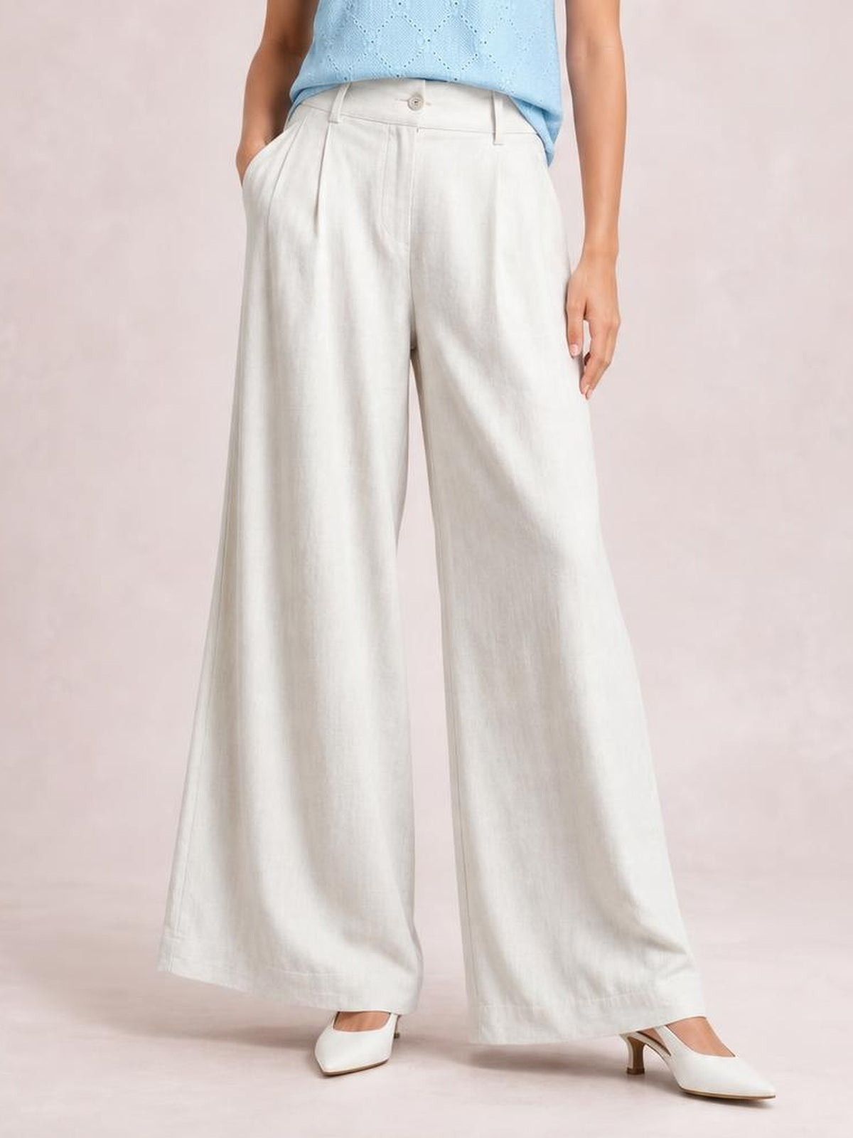 A model wears high-waisted white wide-leg pants with a buttoned waistband, belt loops, front pleats, and side pockets.