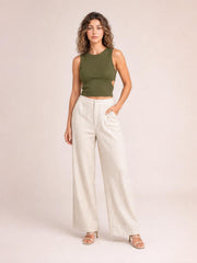 Model poses in cream high-waisted wide-leg pants with front pockets, a button closure, zip fly, and relaxed full-length silhouette.