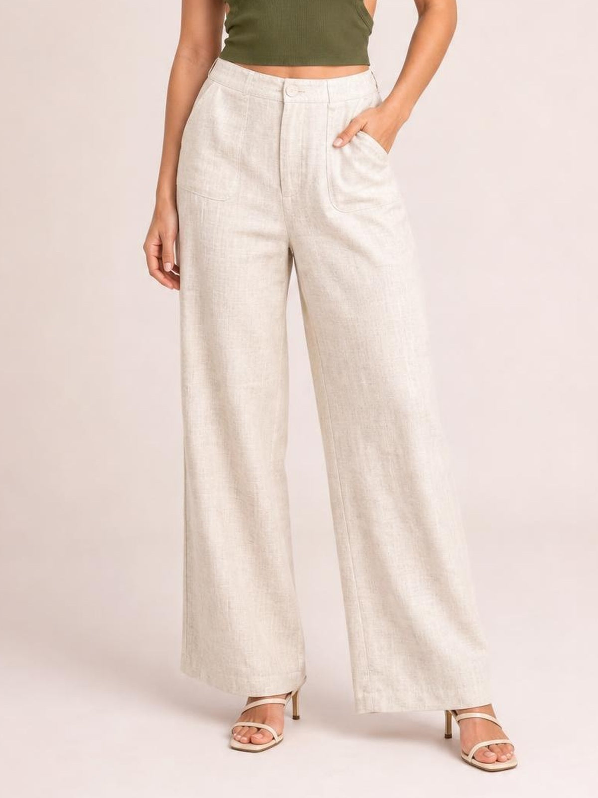 Model wearing high-waisted ivory wide-leg pants with a button closure, front zipper, curved pockets, and a relaxed full-length silhouette.