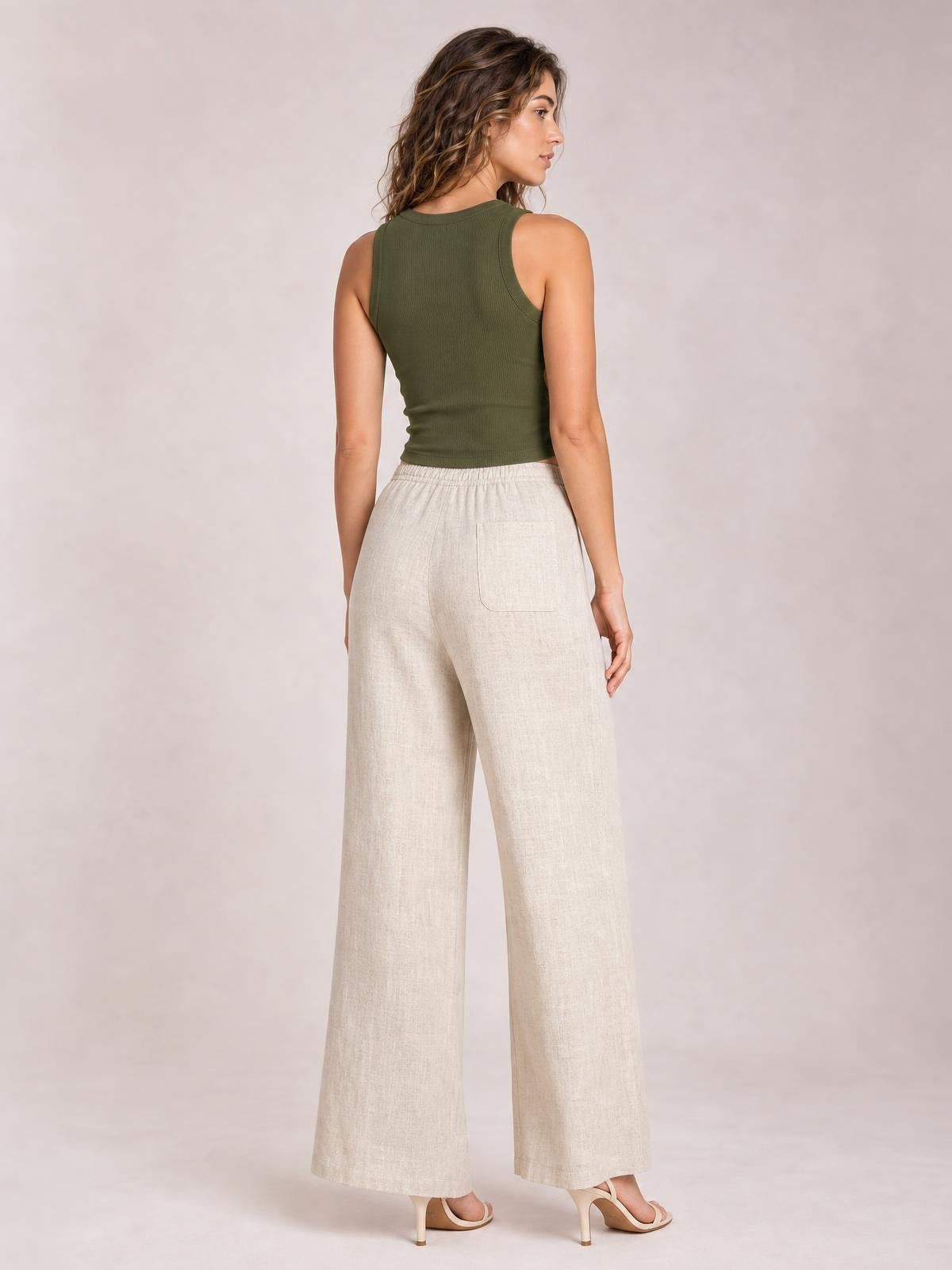 Model shown from the back in high-waisted, wide-leg pants featuring a light beige linen-blend fabric, relaxed silhouette, and back patch pockets.