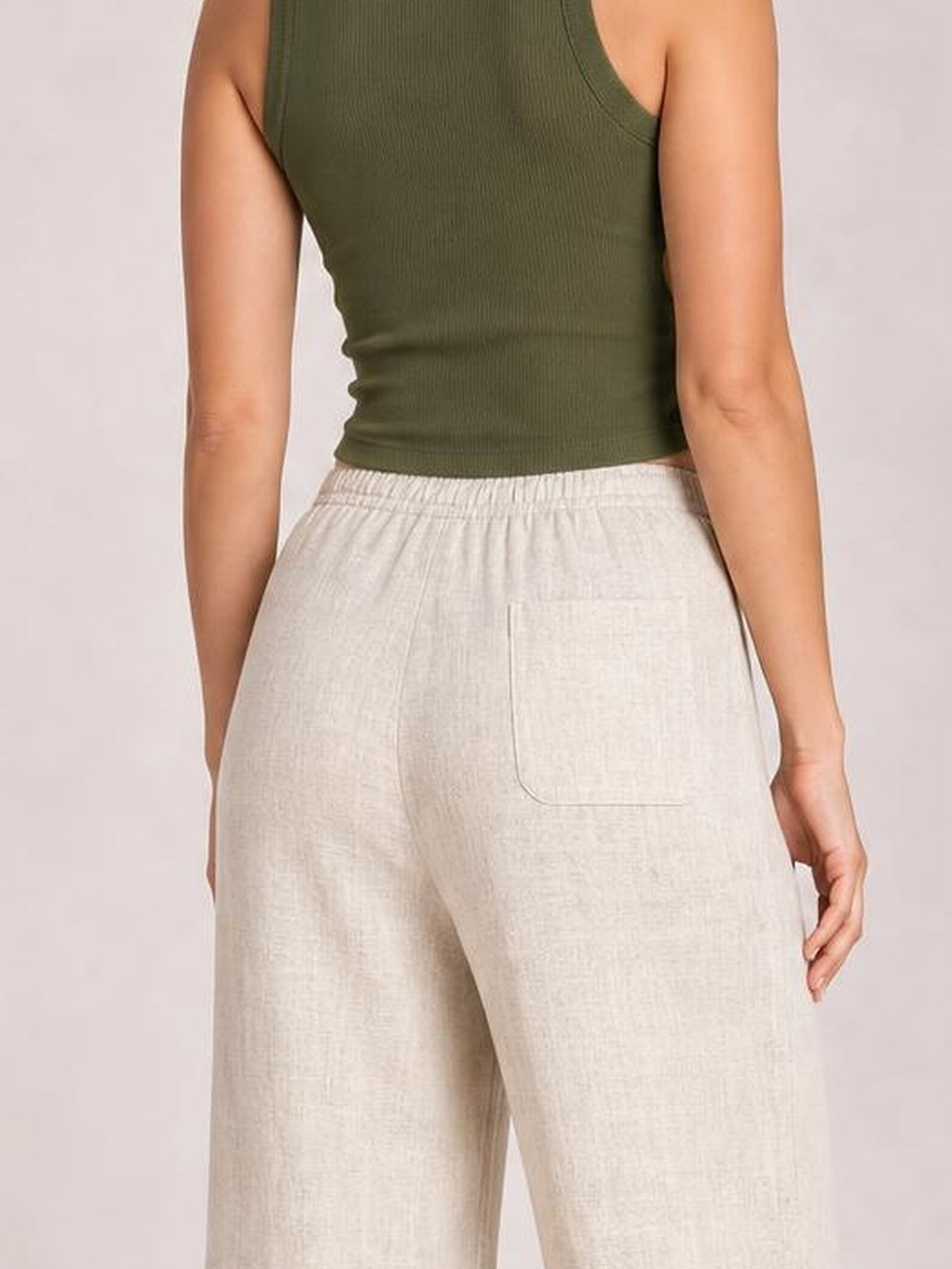 Model shown from the back wearing light beige high-waisted wide-leg pants with a buttoned waist, zipper closure, and large patch pockets.