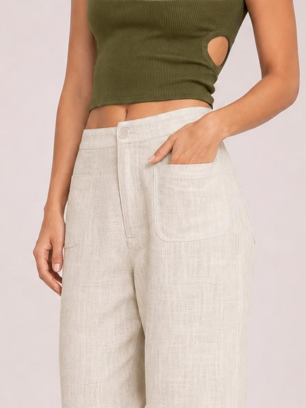Model wears high-waisted wide-leg pants in light natural beige with a button closure, zipper fly, and large front pockets, posing with one hand tucked inside.