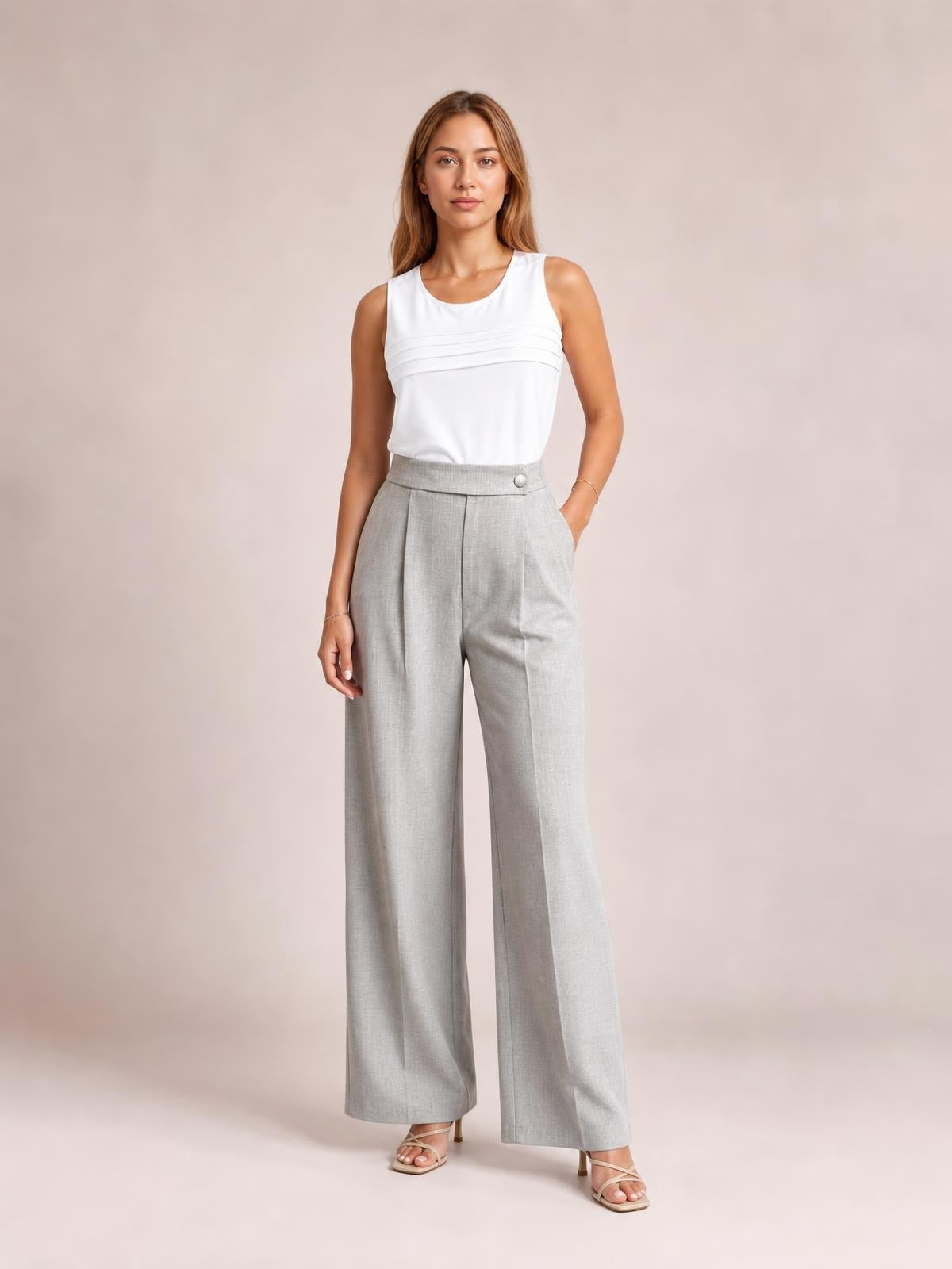 A model stands in light gray high-waisted wide-leg pleated pants with a structured waistband and side pockets, posing with one hand tucked in a pocket.