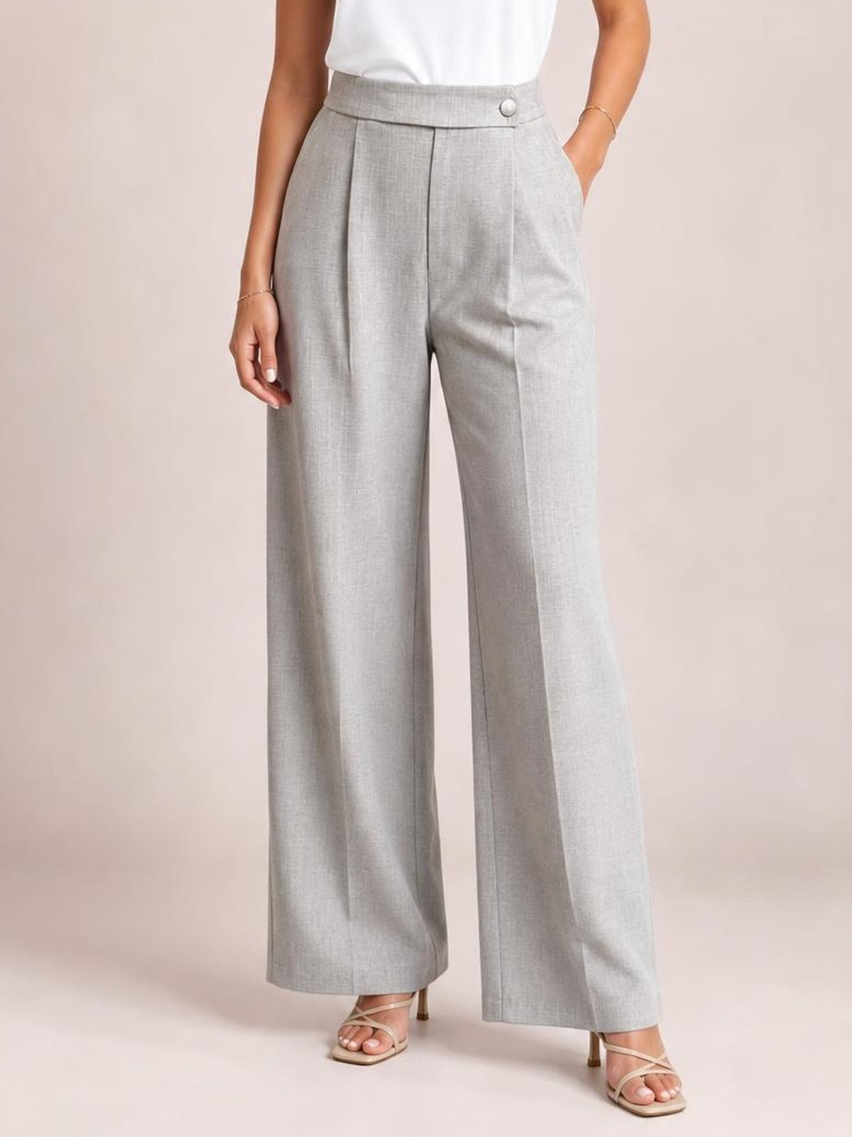 Model wearing light gray high-waisted wide-leg pleated pants with front pleats, a buttoned waistband, side pockets, and a long tailored silhouette.