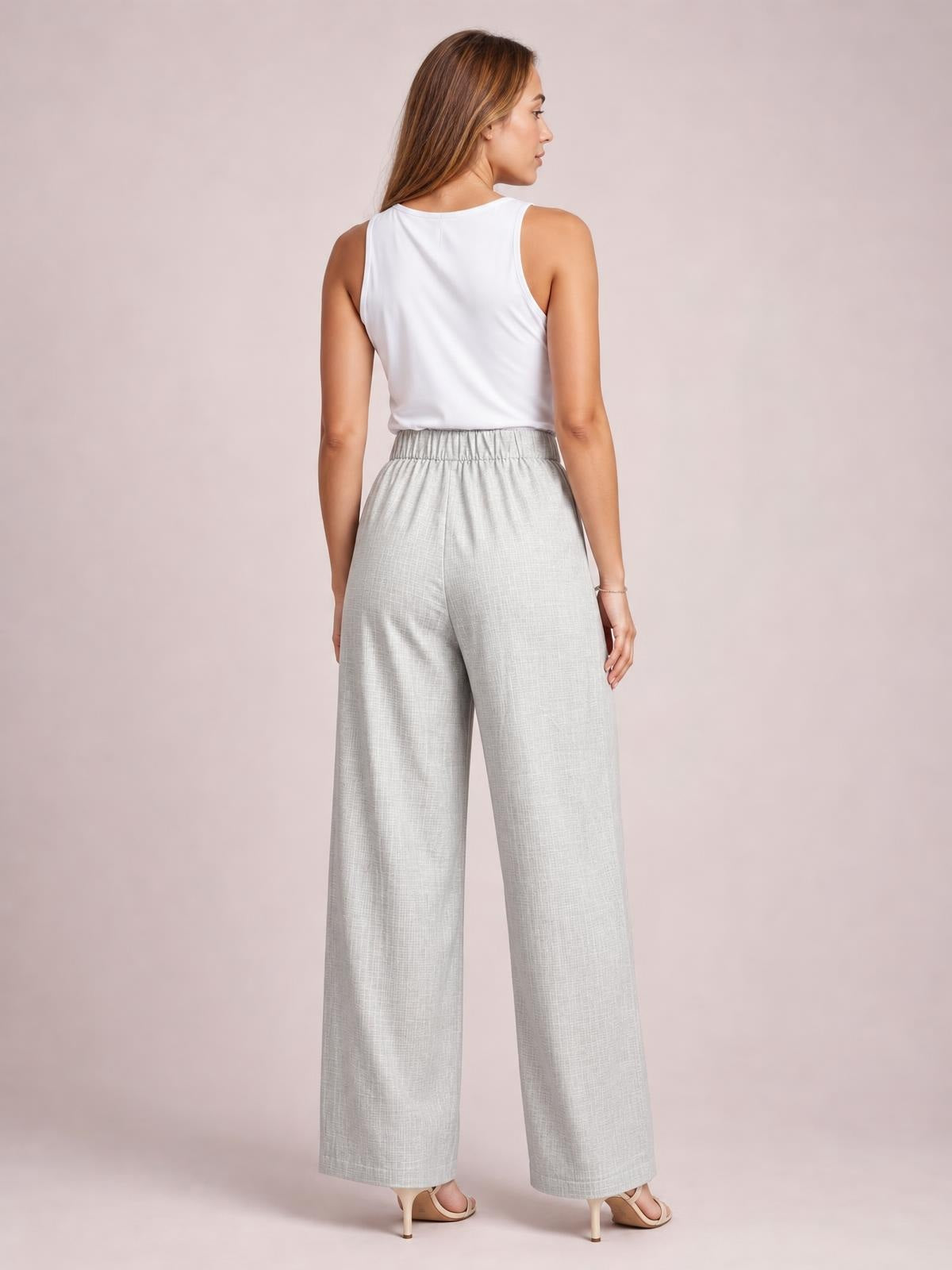 A model shown from behind wears light gray high-waisted wide-leg pants with a gathered waistband and relaxed full-length silhouette, paired with a white sleeveless top.