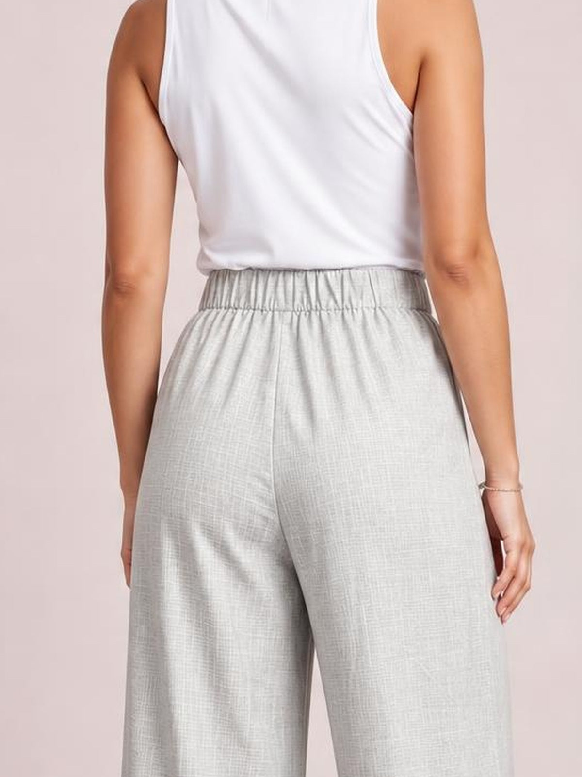 Model shown from behind wearing light gray high-waisted wide-leg pleated pants with a gathered elastic waistband and relaxed, flowing silhouette.