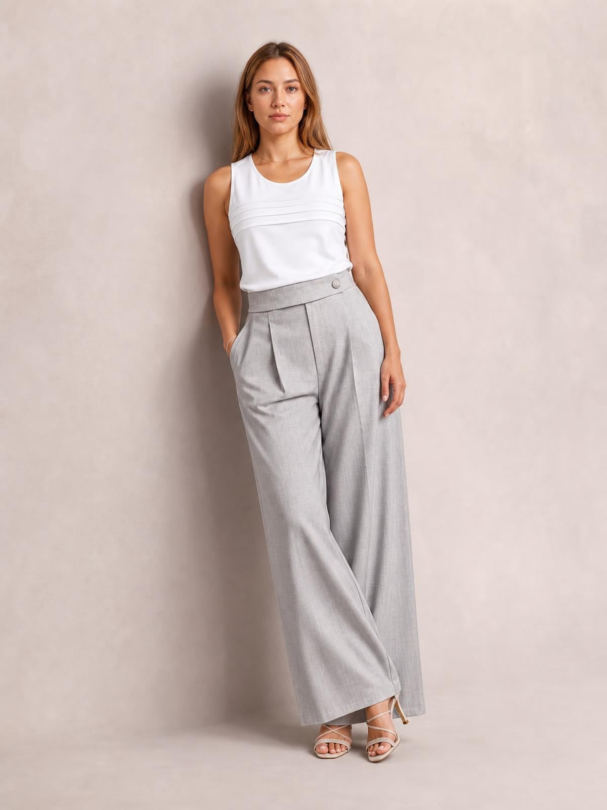 Model poses in light gray high-waisted wide-leg pleated pants with front pockets, a structured waistband, and relaxed flowing silhouette.