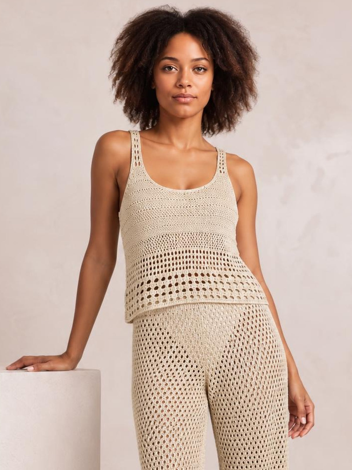 Model stands in a cream sweater cover-up set with a round-neck hollow-out top, sleeveless silhouette, and coordinating openwork pants.