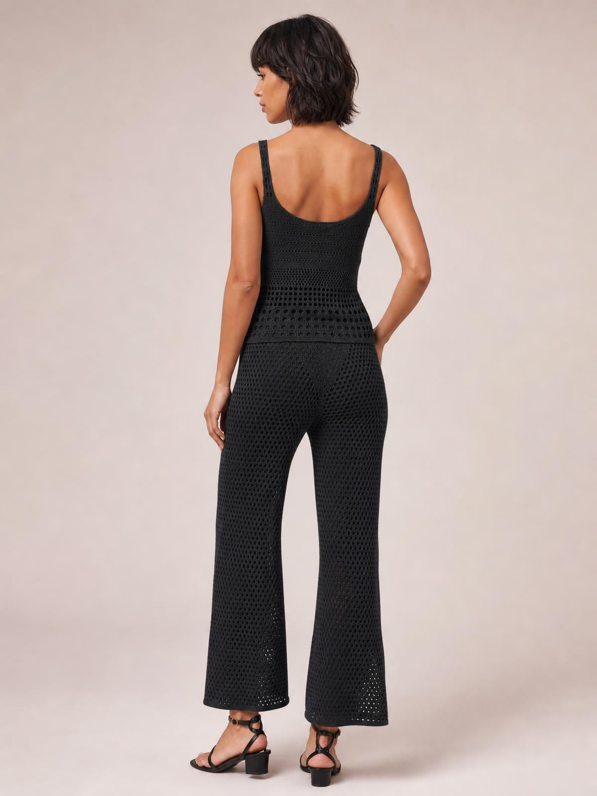 Model poses from behind in a black hollow-out sweater cover-up set with a textured sleeveless top and coordinating wide-leg pants.
