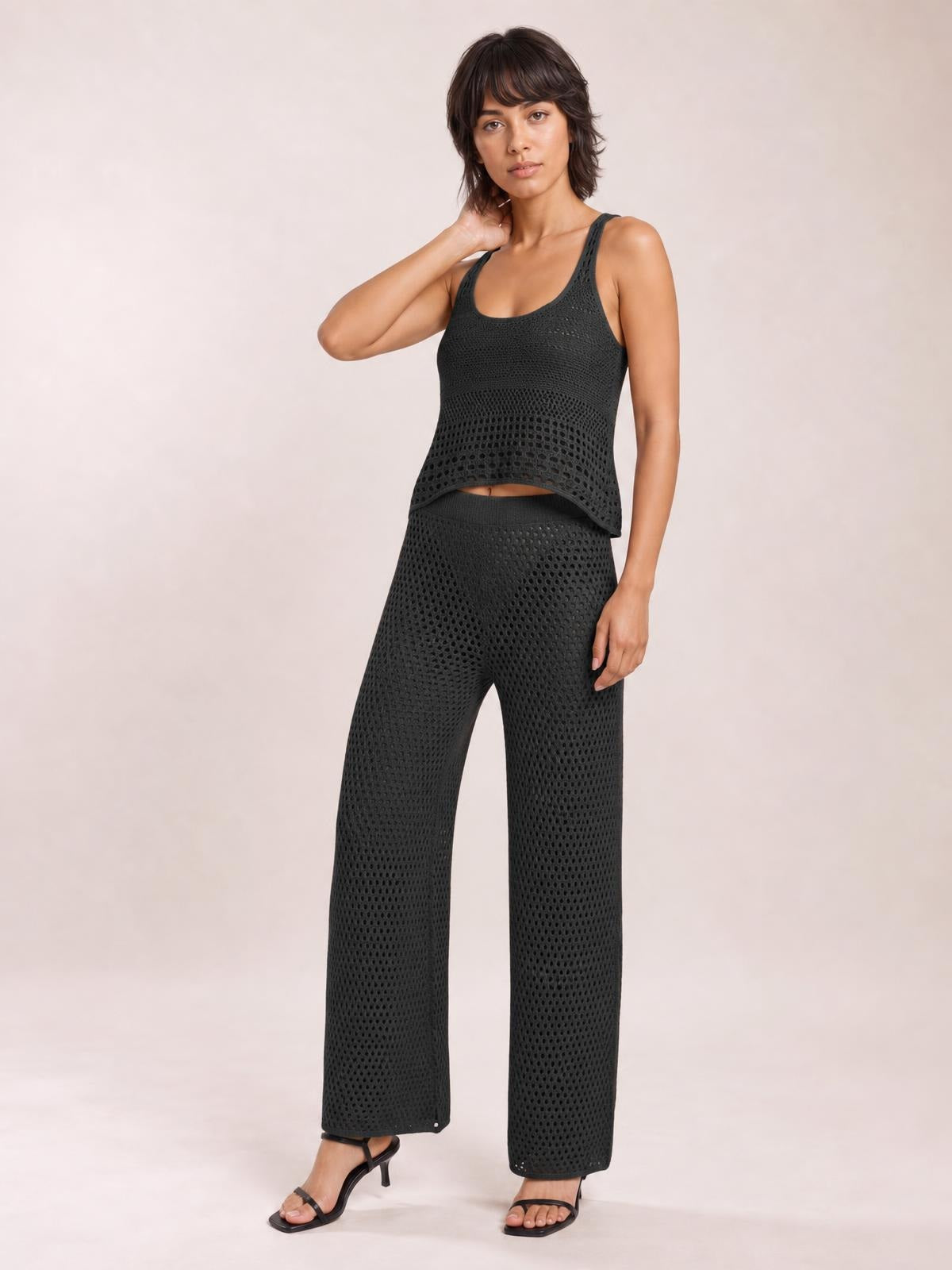 Model poses in a black hollow-out round-neck sweater cover-up top and matching wide-leg pants with openwork knit texture and a relaxed silhouette.