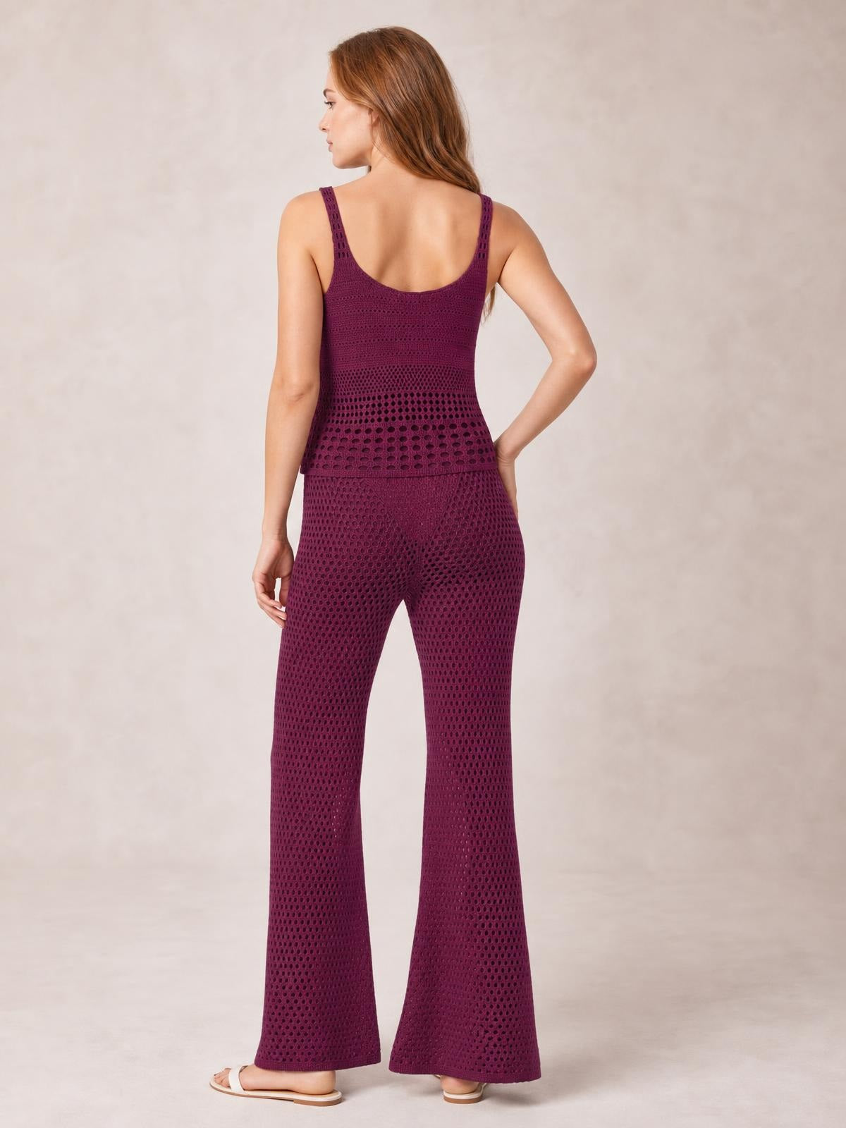Back view of a model in a burgundy hollow-out sweater cover-up set, featuring a scoop back top, textured openwork knit, and wide-leg pants with one hand on her hip.