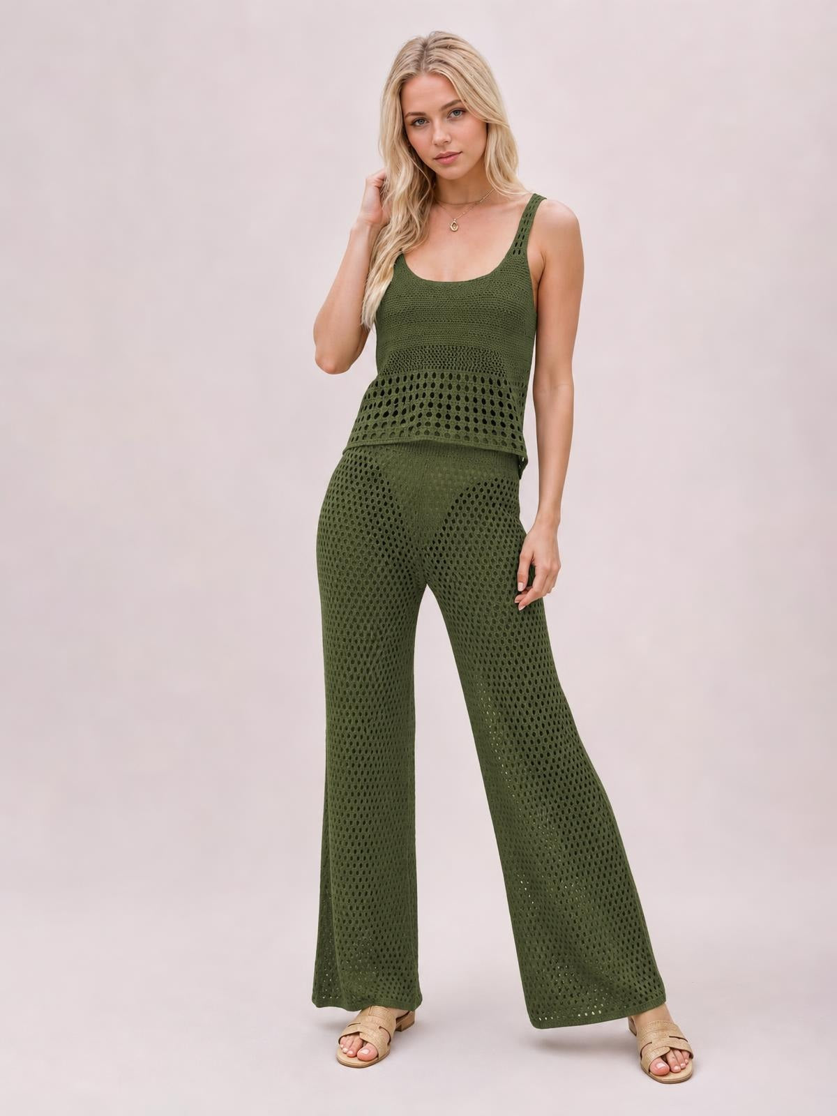 Model wears an olive-green hollow-out sweater cover-up set with a scoop-neck top and matching wide-leg pants, posing with one hand in her hair.