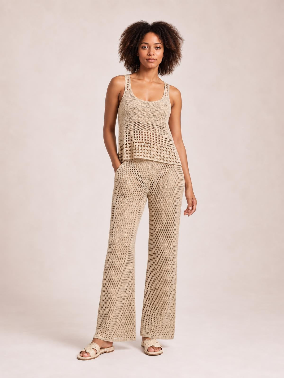 A model poses in a beige hollow-out round-neck sweater cover-up top with a relaxed layered silhouette and coordinating wide-leg openwork pants.