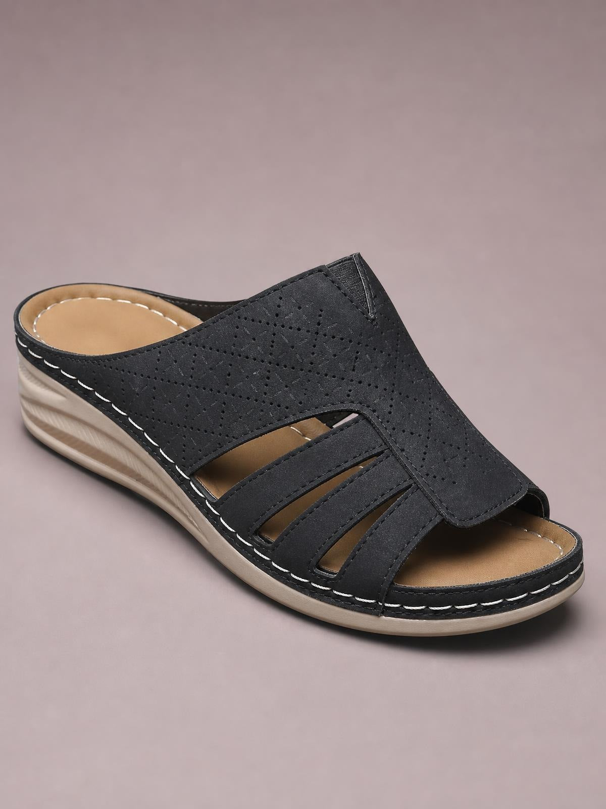 Black hollow-out wedge sandals feature a perforated PU leather upper, layered cutout straps, tan footbed, and a low wedge rubber sole with contrast stitching.