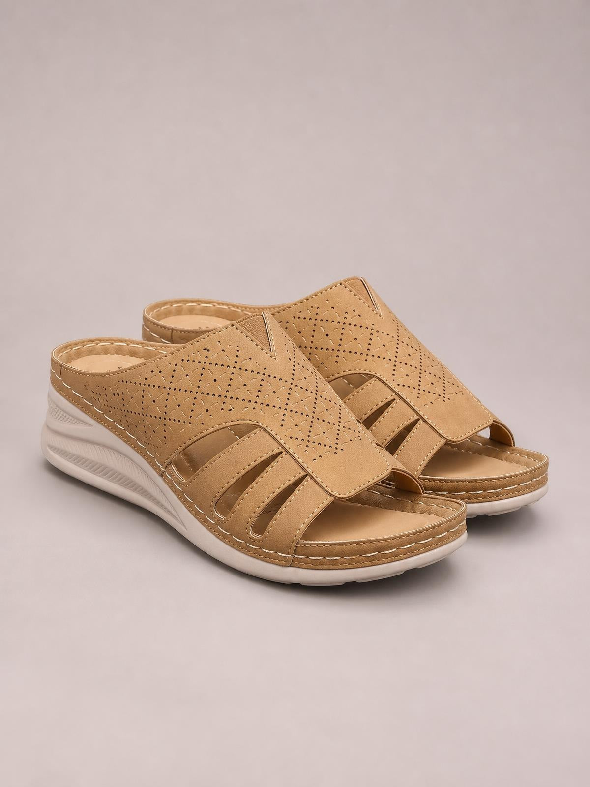 Tan hollow-out wedge sandals feature perforated slip-on uppers, open toes, multiple cutout straps, stitched edges, and cushioned white wedge soles.