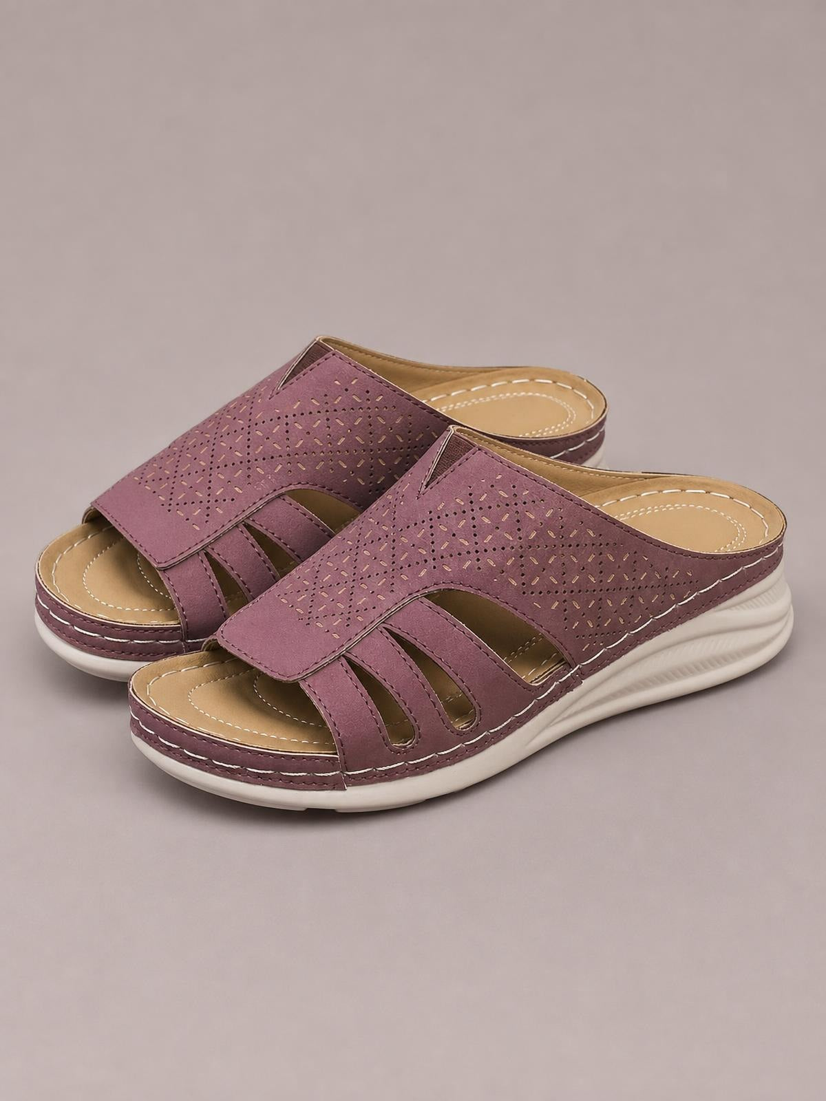 Mauve hollow-out wedge sandals feature open toes, perforated cutout uppers, tan footbeds, stitched detailing, and white textured wedge soles.