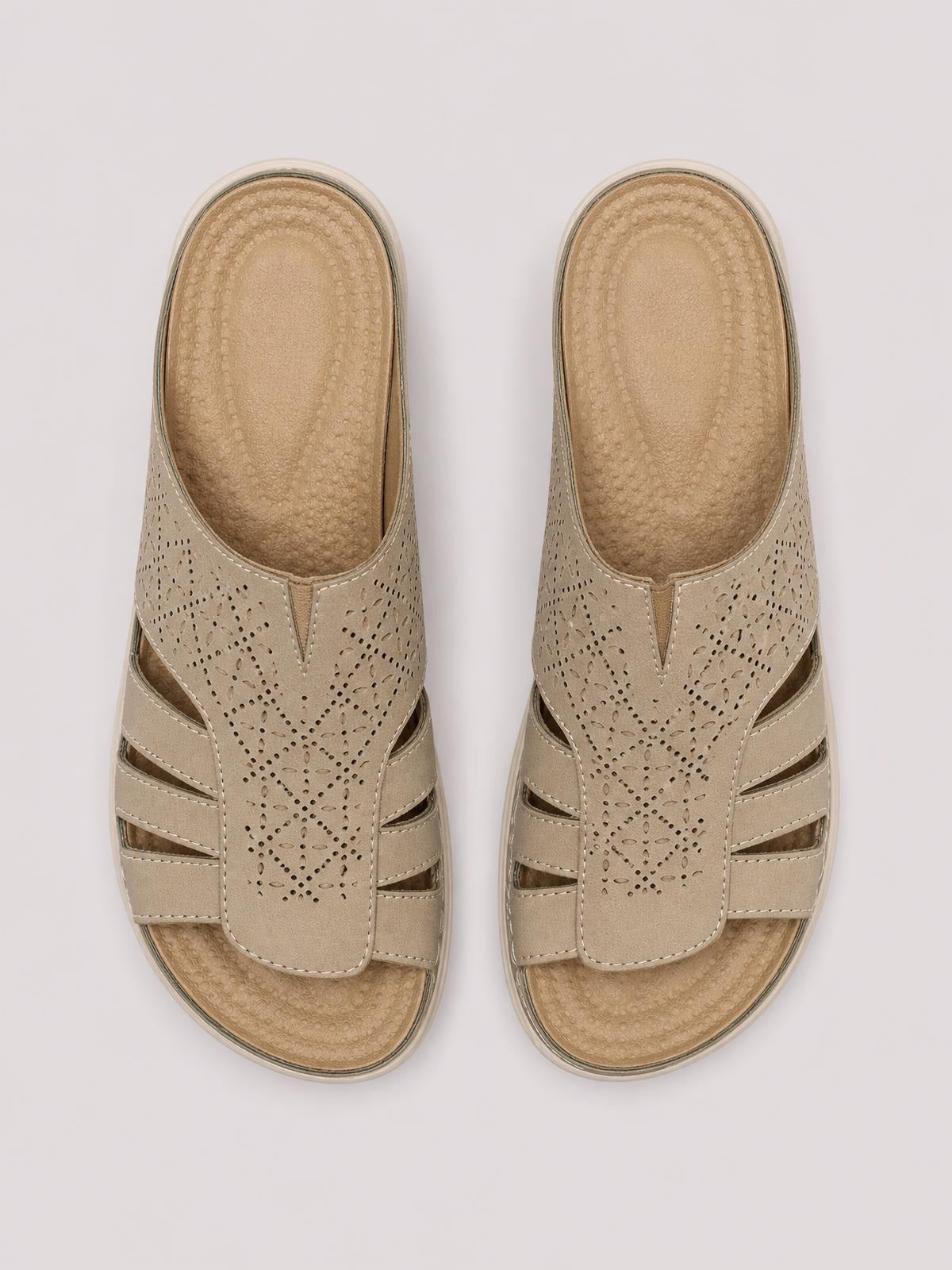 Taupe flat sandals feature perforated hollow-out PU leather straps, layered cutout detailing, cushioned textured footbeds, and durable rubber soles.