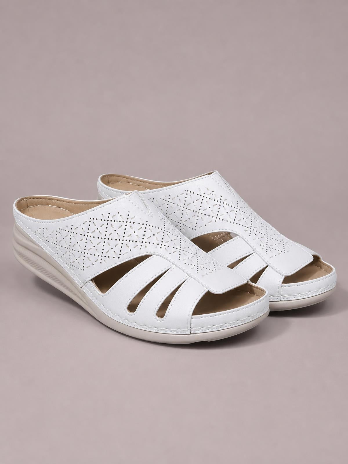 White hollow-out wedge sandals in PU leather feature perforated uppers, crossover cutout straps, open toes, and low rubber wedge soles.