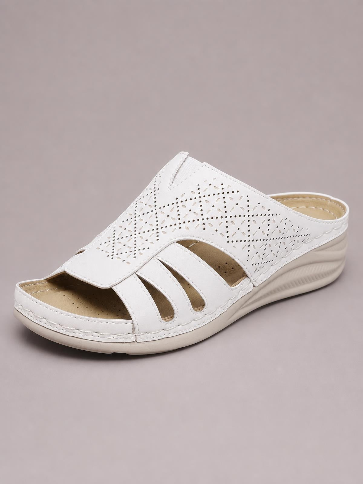 White hollow-out wedge sandals in PU leather feature a perforated upper, open toe, multiple cutout straps, and a low cushioned wedge sole.