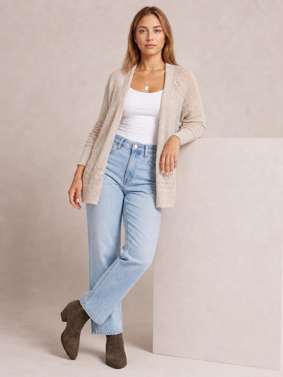 Model wears a cream open front cardigan with hollowed openwork knit, long sleeves, ribbed cuffs, and a relaxed thigh-length silhouette over a white top.