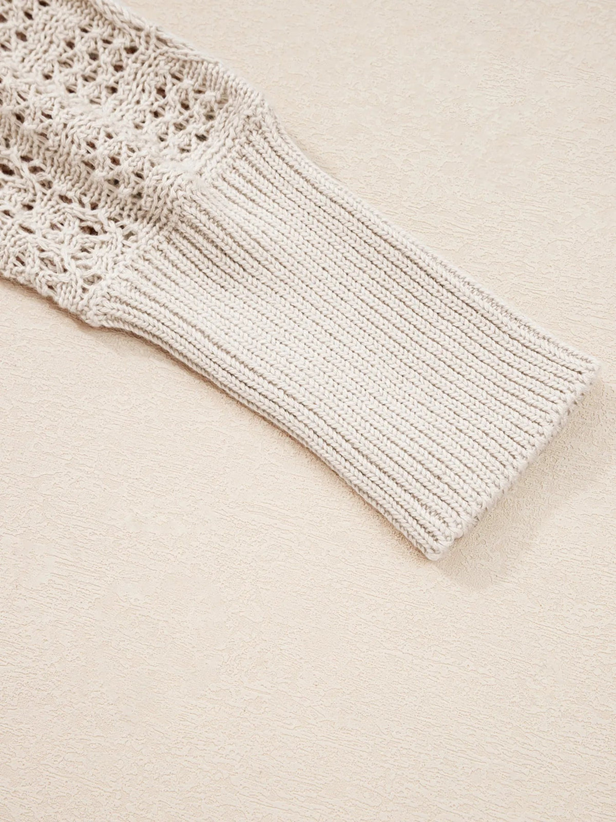 Close-up of an ivory hollowed knit cardigan showing openwork stitching and a wide ribbed sleeve cuff with a softly textured construction.