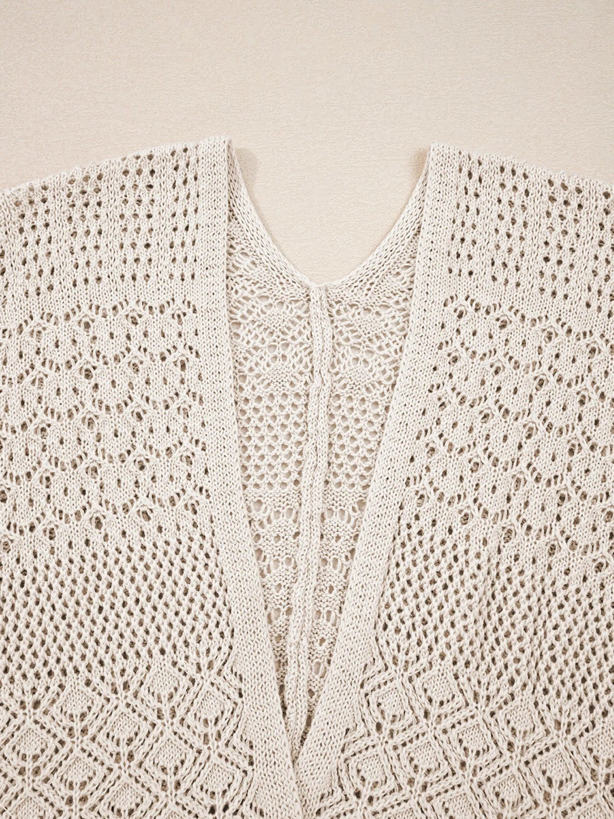 Close-up of a cream hollowed knit cardigan showing its open front, intricate openwork stitch pattern, and textured panels.
