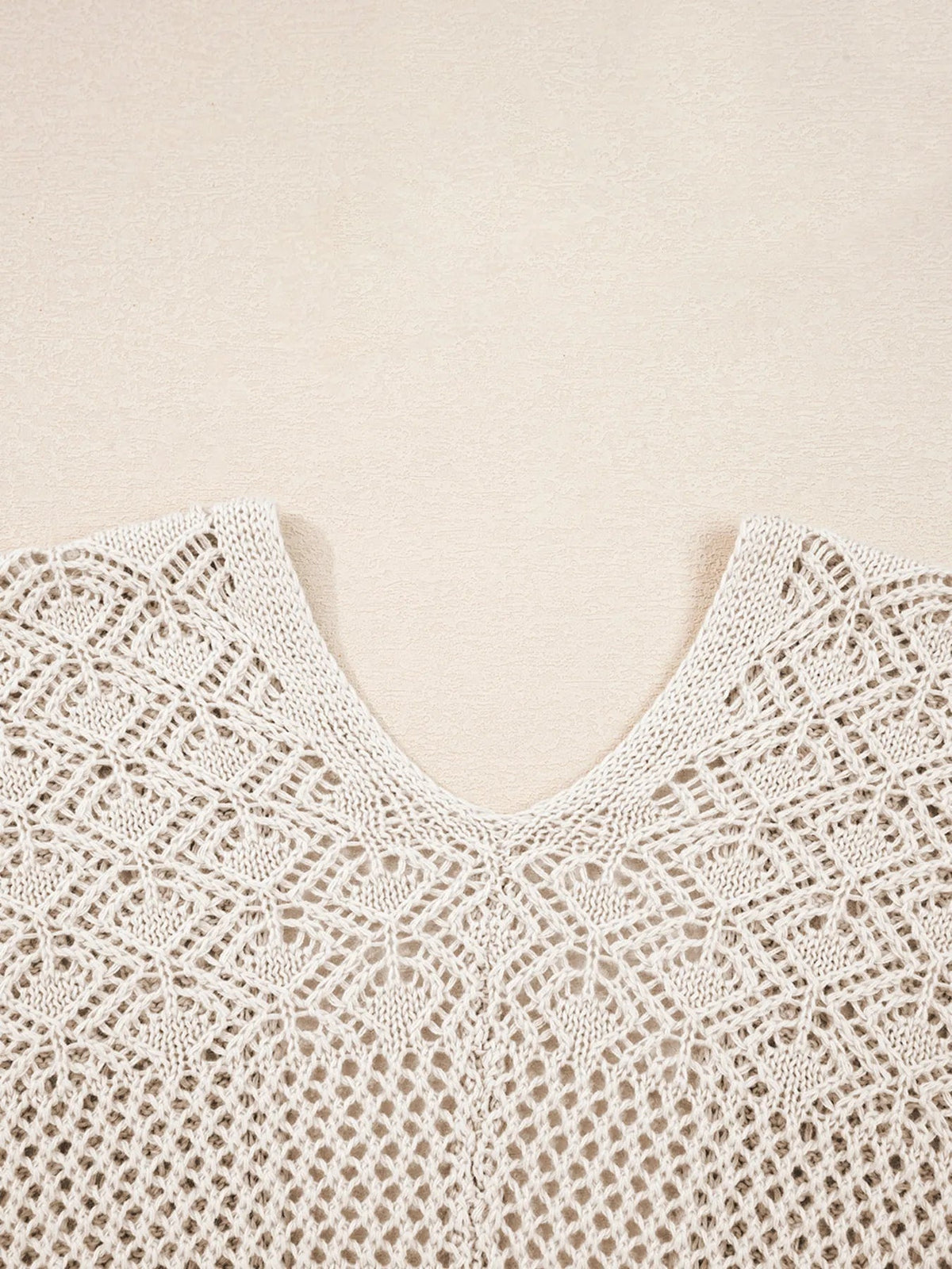 Close-up of a cream hollowed knit cardigan featuring an airy openwork diamond pattern, textured stitching, and neatly finished solid-knit edges.