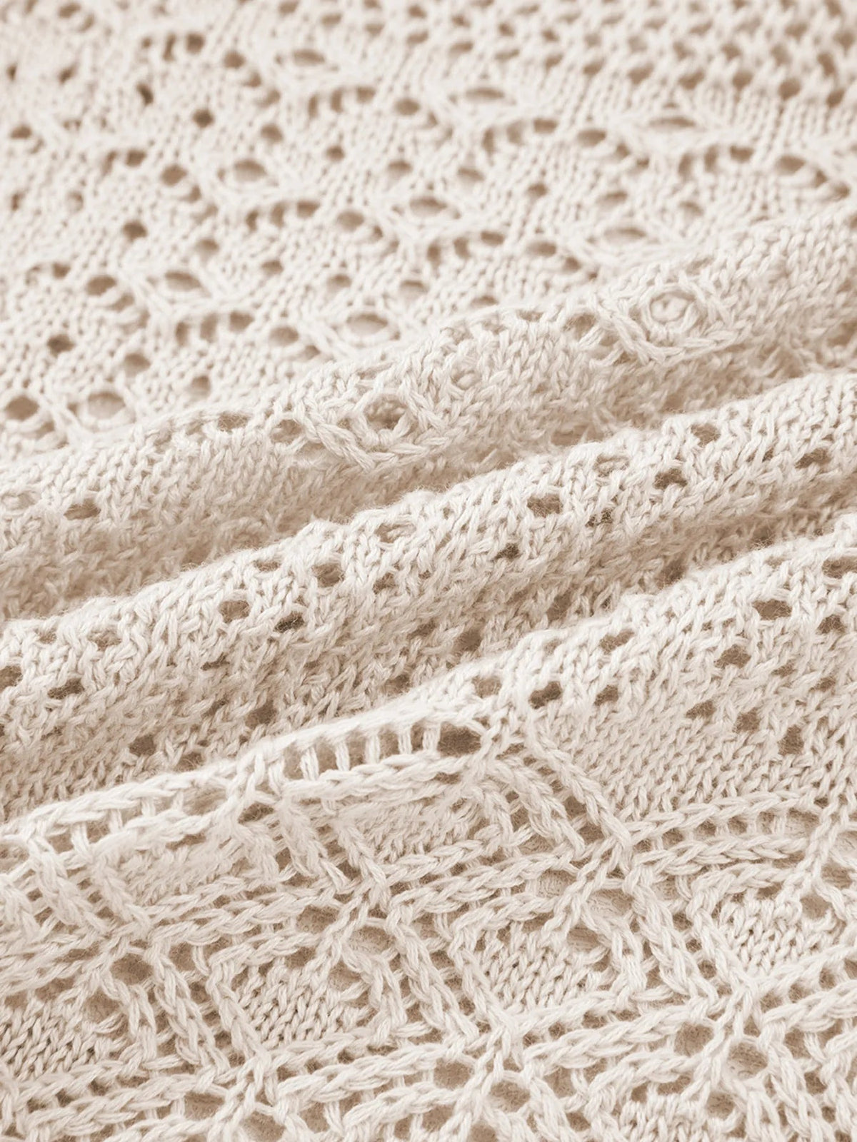 Close-up of a cream openwork knit cardigan showing its textured yarn, hollowed weave, and layered construction.