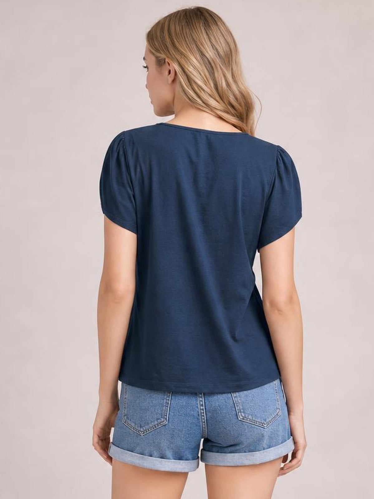Back view of a model wearing a navy short sleeve blouse with a relaxed straight silhouette, rounded neckline, and softly gathered shoulder seams.