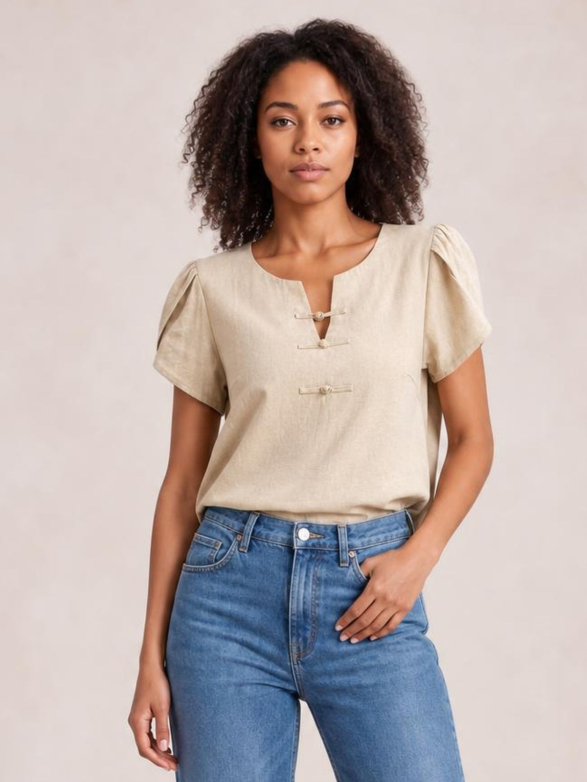 Model wears a honey notched short sleeve blouse with a relaxed silhouette, gathered shoulders, and two front toggle closures, paired with jeans.