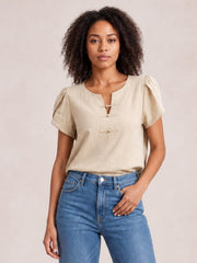 Model wears a honey notched short sleeve blouse with a relaxed silhouette, gathered shoulders, and two front toggle closures, paired with jeans.