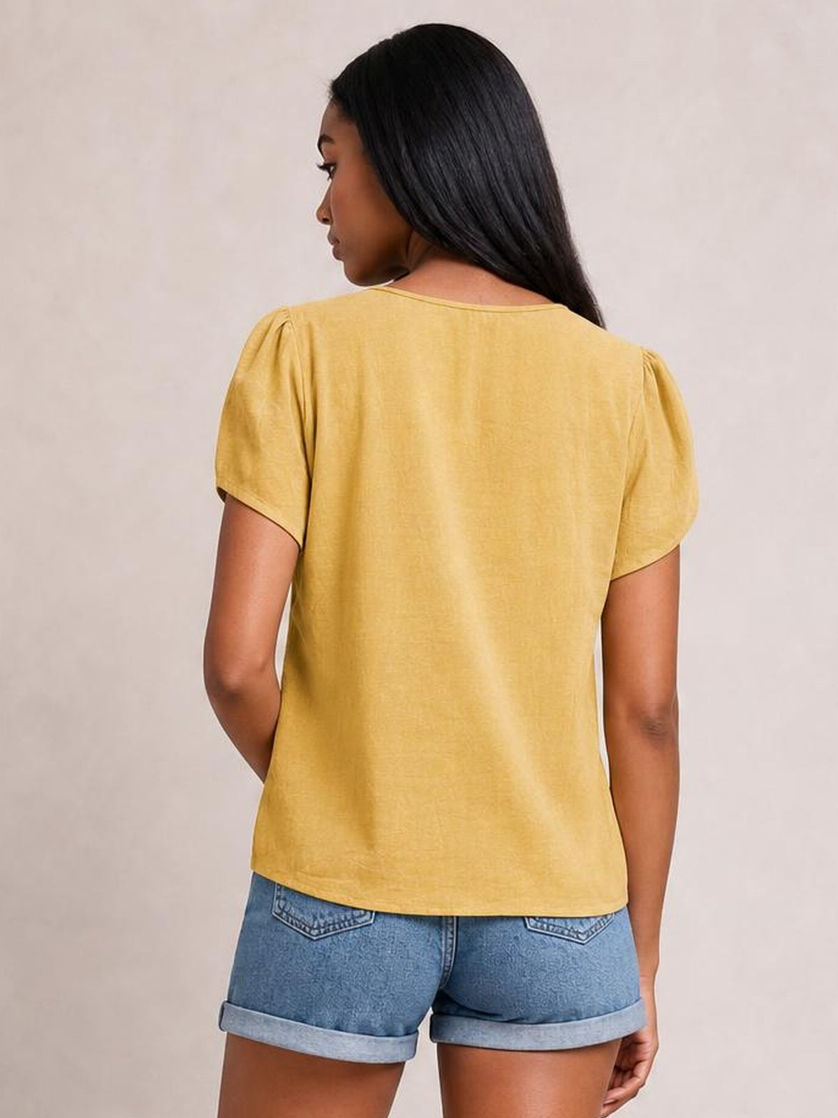 Model seen from behind wearing a honey yellow notched short sleeve blouse with a relaxed straight silhouette and clean sleeve hems.