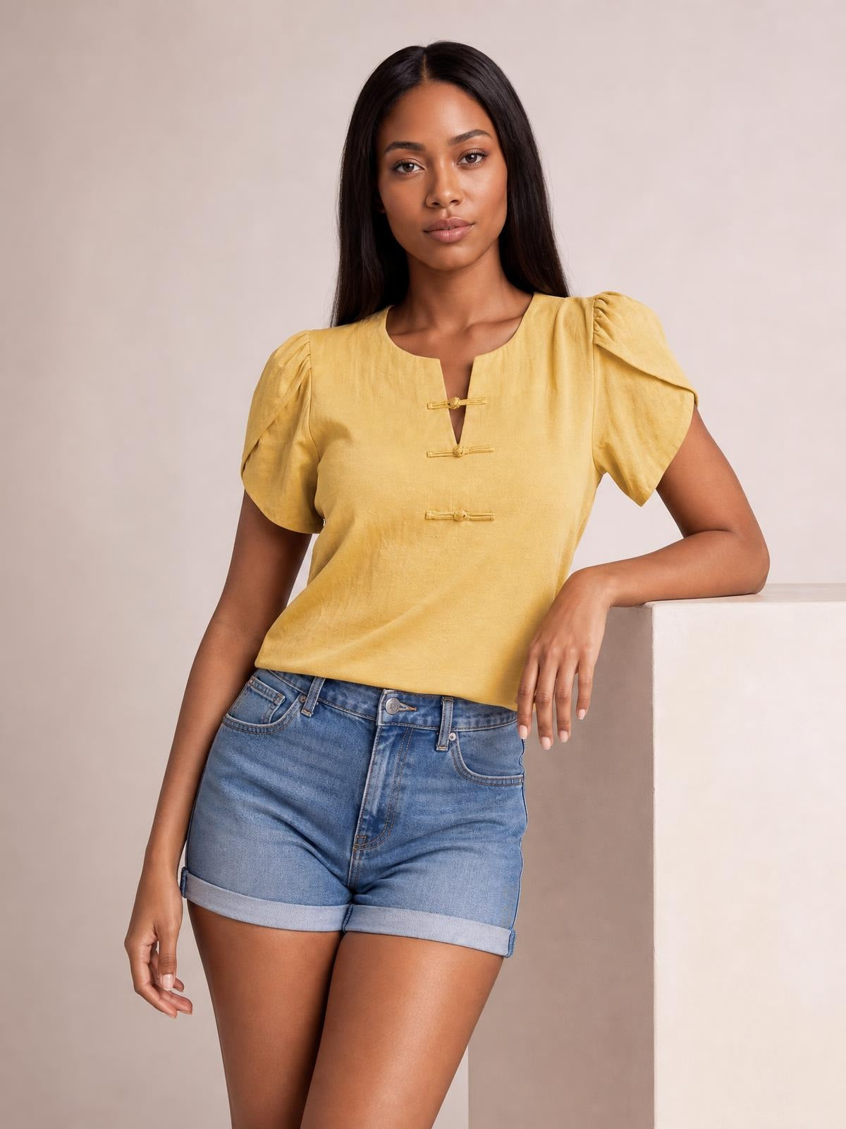 Model wears a honey yellow notched short sleeve blouse with gathered shoulders, a relaxed straight silhouette, and three front loop closures.