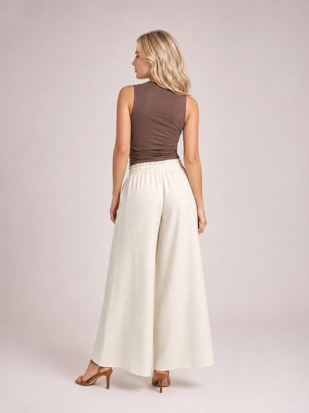 Back view of a model wearing opaque ivory high-waist wide-leg pants with a gathered waistband and flowy full-length silhouette.