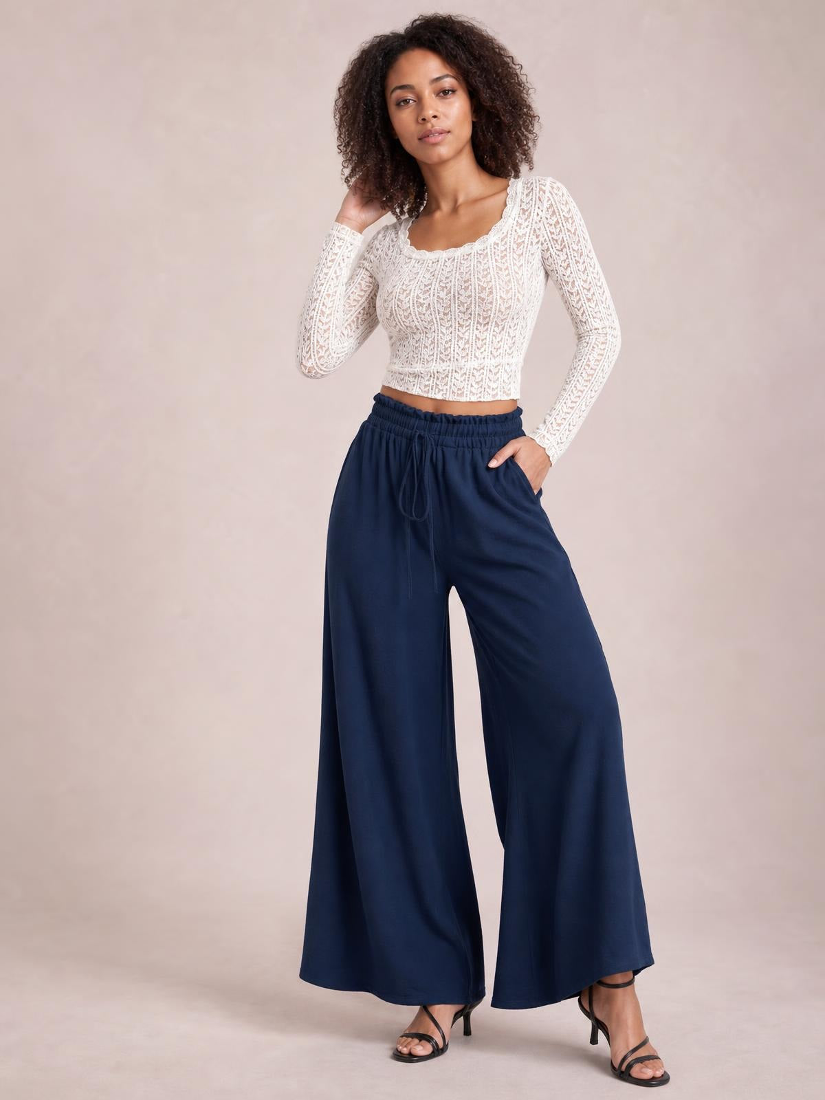 Model poses in navy tied high waist wide leg pants with a drawstring waistband, flowing full-length silhouette, and relaxed drape.