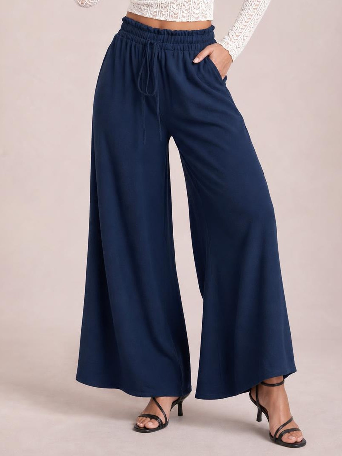 Model wearing navy tied high waist wide leg pants with a gathered elastic waistband, front drawstring, flowing silhouette, and side pockets.