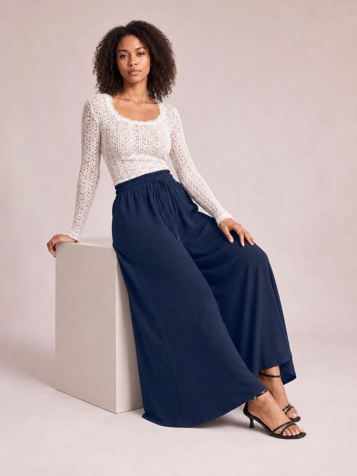 Model seated in navy tied high-waist wide-leg pants with a flowing silhouette, elastic waistband, and drawstring closure.
