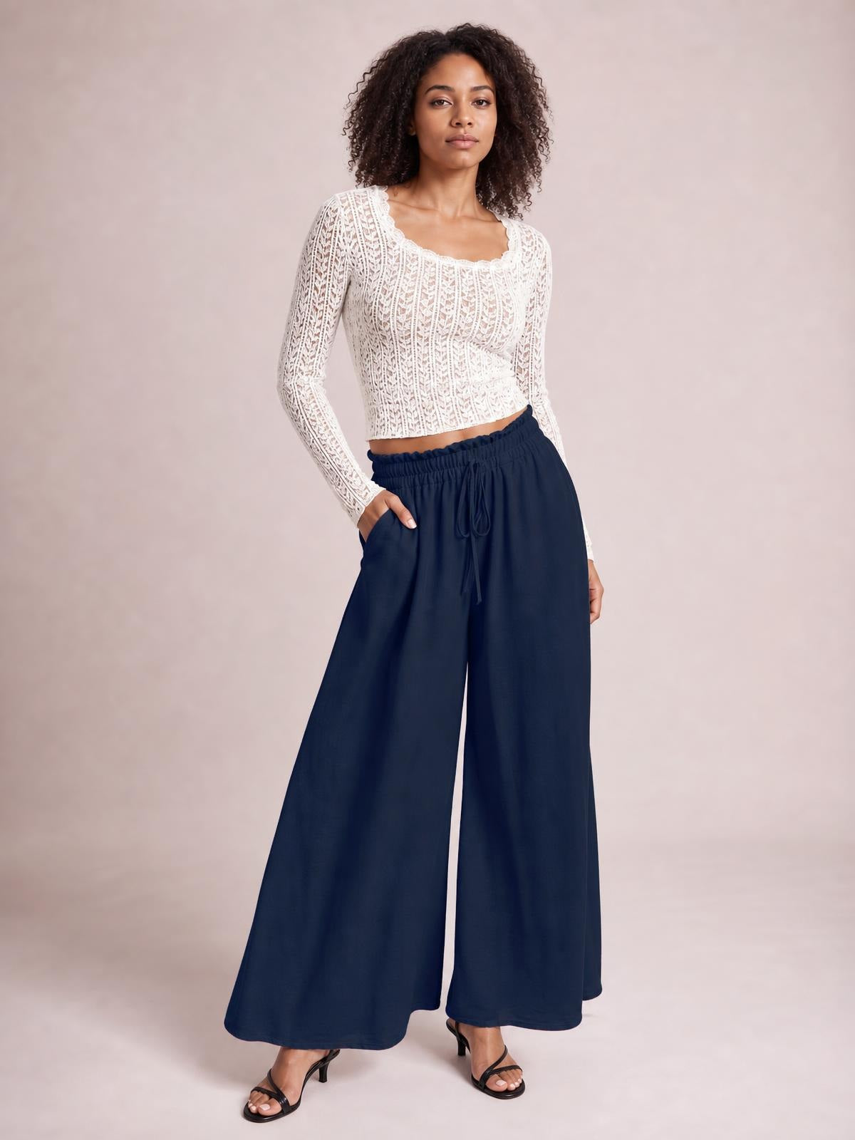 A model poses in navy tied high-waist wide-leg pants with an elastic waistband, drawstring front, flowing silhouette, and one hand in a pocket.