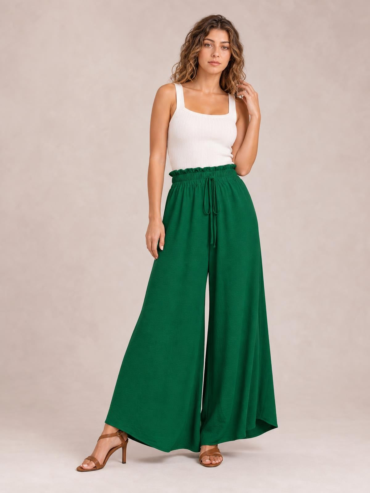 Model poses in deep green tied high-waist wide-leg pants with a gathered waistband, long flowing silhouette, and front drawstring.