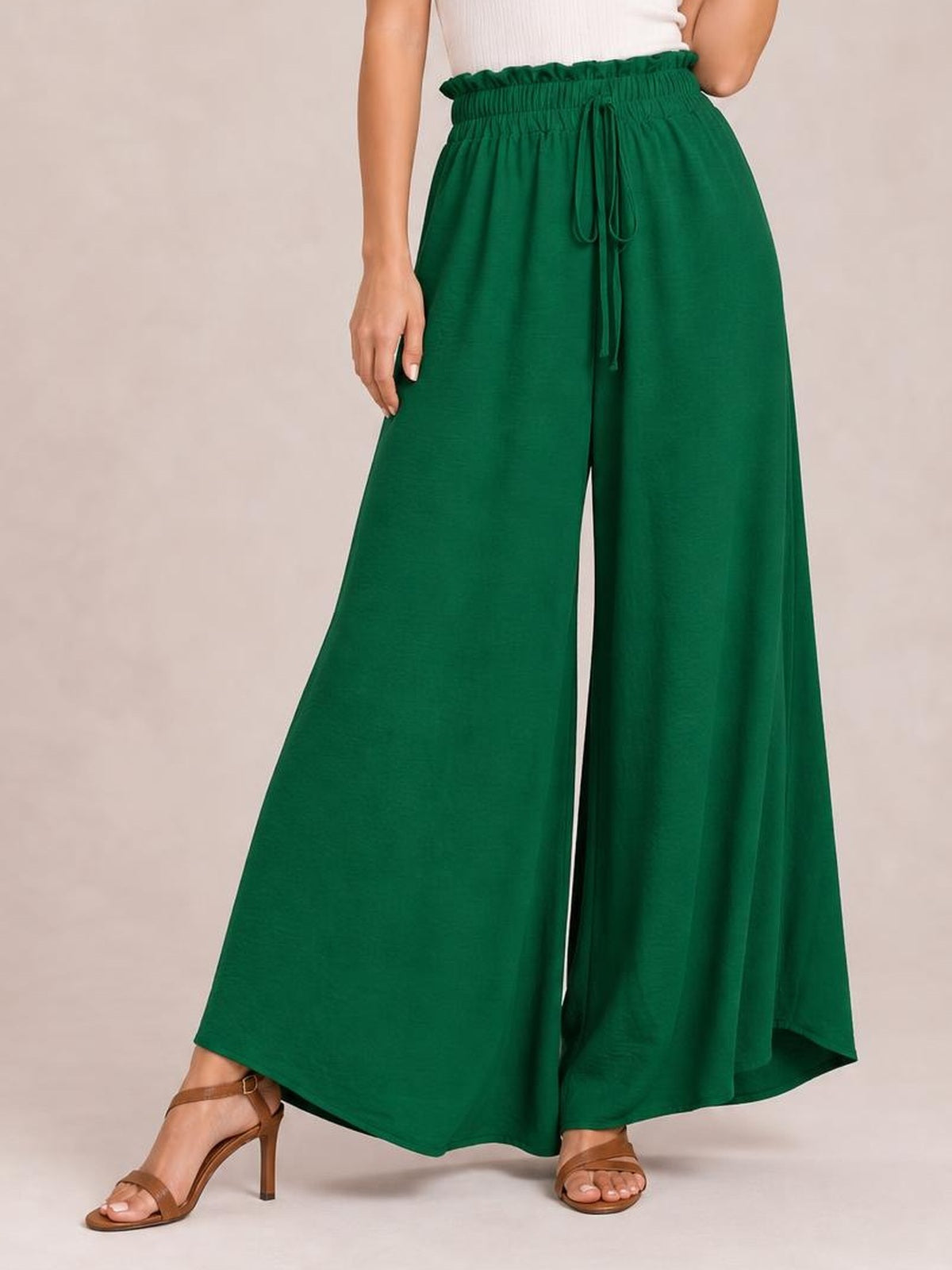 A model wears deep green tied high waist pants with a gathered waistband, drawstring front, opaque flowy fabric, and an extra-wide leg silhouette.