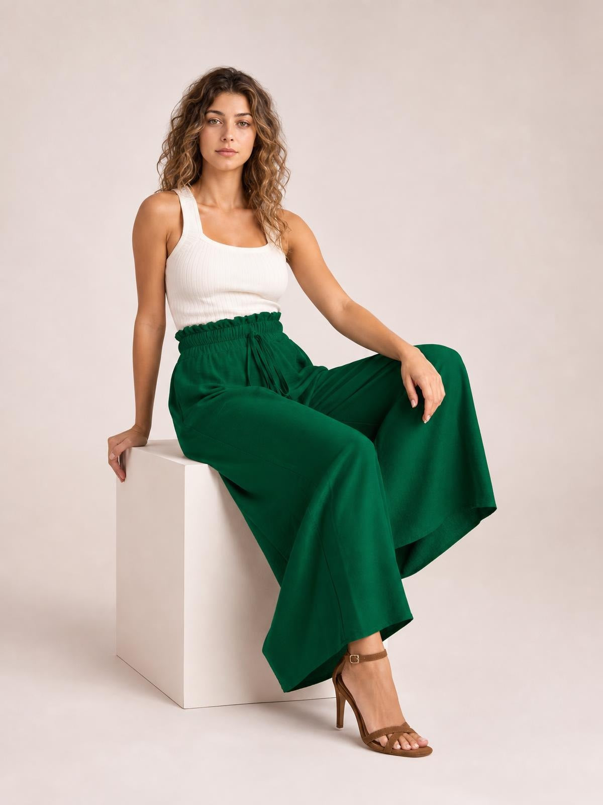 Model seated in emerald green tied high waist wide leg pants with a gathered waistband and flowy, relaxed silhouette.