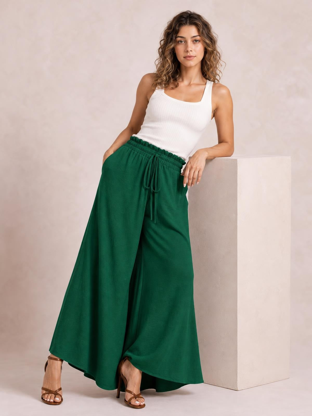 Model wearing emerald green tied high-waist wide-leg pants with a gathered waistband, front drawstring, flowing silhouette, and full-length construction.