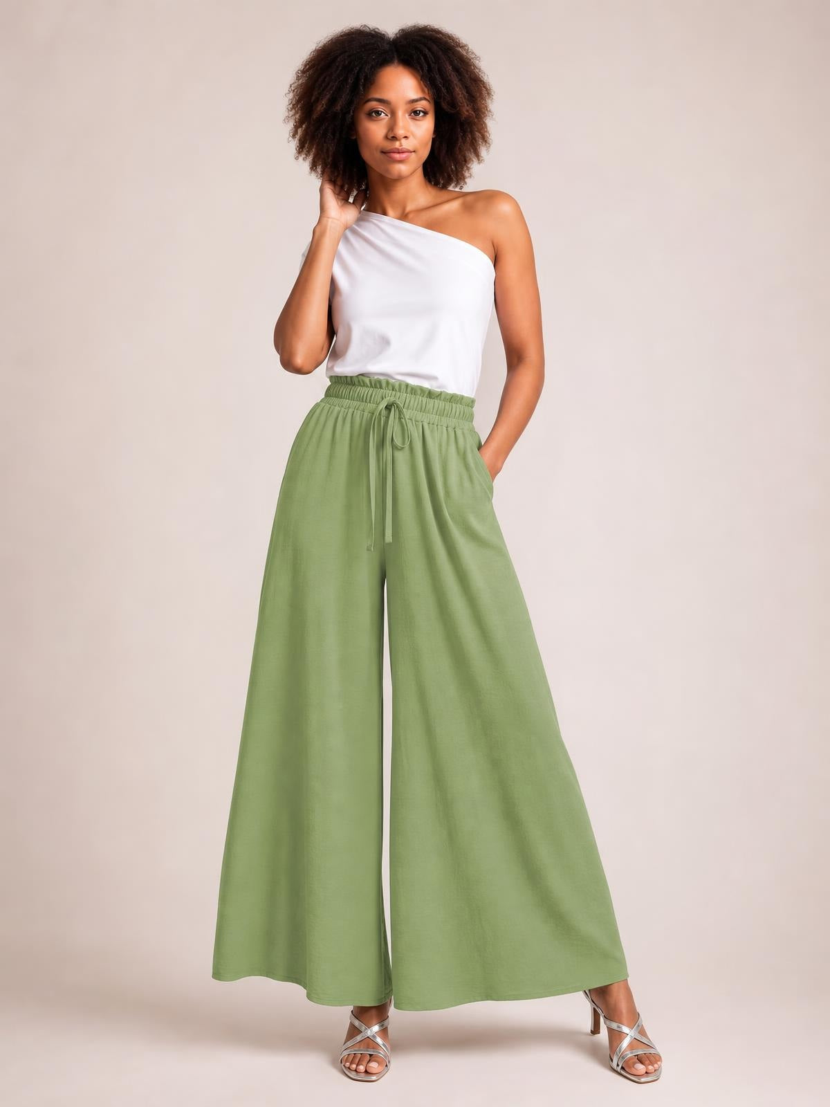 Model poses in sage green tied high-waist wide-leg pants with a gathered elastic waistband, drawstring front, flowing silhouette, and side pockets.