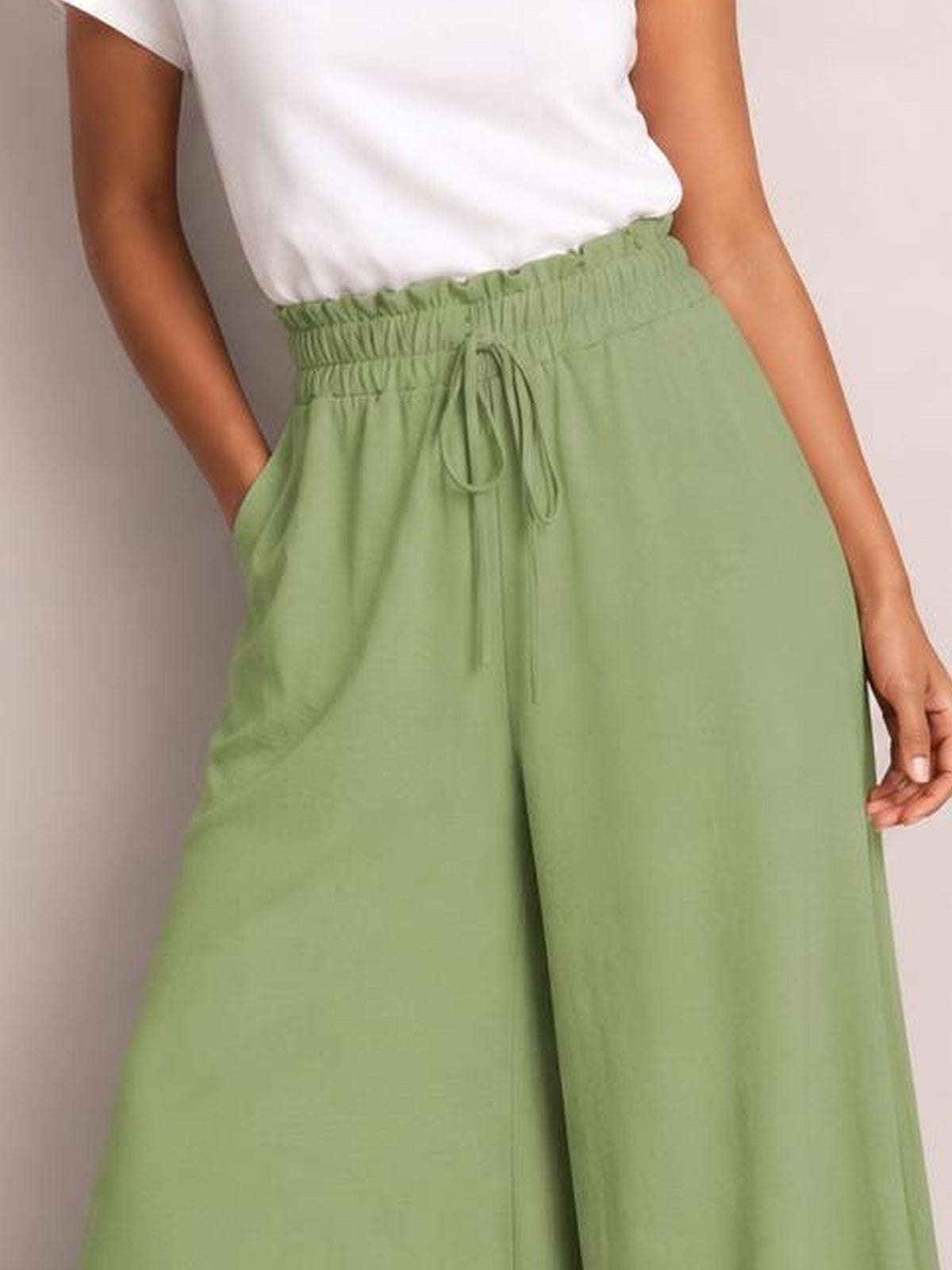 Model wearing sage green tied high waist wide leg pants with an elastic waistband, drawstring front, and relaxed flowing silhouette.