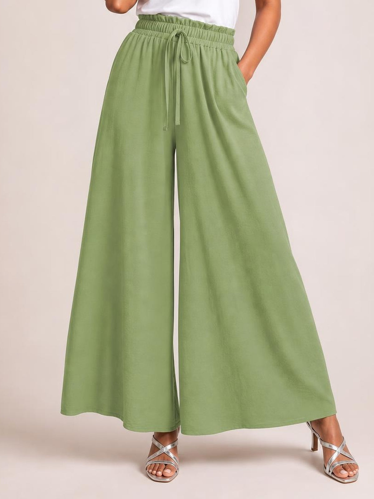 Model wearing sage green tied high-waist wide-leg pants with a gathered waistband, drawstring, side pockets, and flowing opaque silhouette.